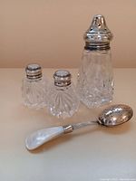 Photo of the muffineer, tea infuser spoon, salt and pepper shakers showing cut glass bodies and sterling silver tops/handle.