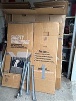 Three U-Haul Shorty Wardrobe cardboard boxes with metal support bars in front, boxes stacked upright in garage or storage space