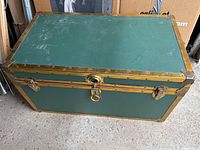 Top view of the rectangular green metal trunk with gold trim showing surface wear and lock on front.