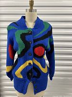 Front view of vintage knit sweater jacket showing bold abstract colorful design on bright blue background and button closure.