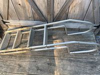 Full view of the aluminum pool ladder showing the two wide steps and curved handrails, placed against a wooden fence on a wood deck.