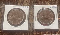 Photo showing both 1968 and 1982 Canadian silver dollar coins in protective holders with year labels.