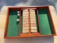 Top view of wooden tray with green felt compartments, central scoring track, and three dice
