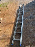 Full view of 24-foot aluminum extension ladder on ground outdoors, showing two extendable sections and blue protective end caps.