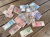 Overview of the foreign currency banknotes laid out on a wooden surface, showing several notes with visible text and portraits from various countries including Peru, Costa Rica, Mexico.