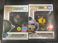 Photo of Assaultron figure in original box, numbered 386, with glow-in-the-dark sticker and Fallout convention exclusive sticker visible.