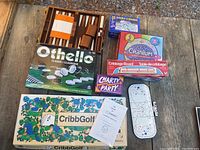 Overview of the 8 game boxes and boards arranged on wooden surface showing Othello, Cribbage, Cranium, CribbGolf, CharTy Party, Dominoes, and hockey peg game