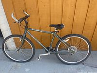 Side view of the green Giant Boulder 550 mountain bike showing frame, tires, seat, and handlebars against orange wooden wall.
