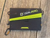 Closed Goal Zero Nomad 7 solar charger showing black fabric case with lime green diagonal stripe and logo, orange carabiner attached.