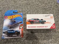 Photo showing two Hot Wheels 1970 Dodge Charger R/T cars, one in carded blister packaging and one in Hot Wheels id box.