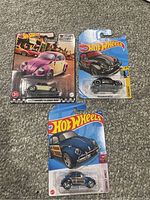 Three Hot Wheels Volkswagen Beetle toy cars in original packaging, shown on carpeted floor.