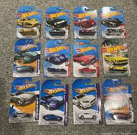 Overview of all 12 Hot Wheels cars in original blister packs arranged in a 4x3 grid on carpeted floor showing variety of colors and models