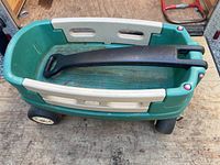 Green and beige plastic kids wagon with black handle and four wheels, shows minor signs of use.