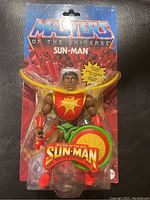 Front view of the Masters of the Universe Sun-Man action figure in original sealed packaging, showing figure and accessories clearly.