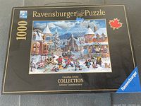 Box front showing Ravensburger brand, 1000 pieces, Canadian Artists Collection, winter village scene with a maple leaf symbol.