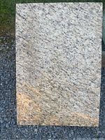Full view of the rectangular natural stone slab placed on gravel, showing beige and black mottled texture with some orange areas.