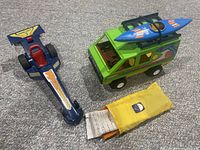 Photo showing blue drag race car, green camper van with rooftop kayak, and yellow sleeping bag in front.