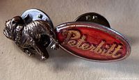 Close-up photo of the Peterbilt oval logo cuff link showing red and gold enamel with metal backing.