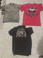Three vintage t-shirts laid out: gray Nickelback, red Americas Lake George, black Harley Davidson Staff