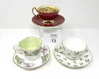 Three Aynsley bone china tea cups and matching saucers, each with a distinct pattern and gold trim, displayed together.