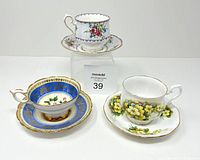 Three bone china teacups and saucers displayed on white surface with lot marker visible.