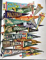 Overhead view of six assorted felt pennants including Aloha, Mackenzie, Orillia, Iroquois, Whitby, Saint John