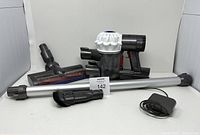 All vacuum components including main handheld vacuum, extension wand, brush heads, and charger shown together.