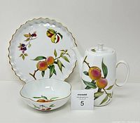Three-piece Royal Worcester Evesham set including coffee pot with lid, flan dish, and small bowl all showing fruit and foliage patterns with gold trim.