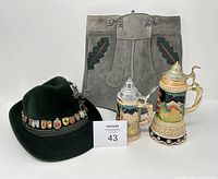 Two ceramic beer steins, green felt Oktoberfest hat with pins, and vintage boys suede shorts in tan and green.