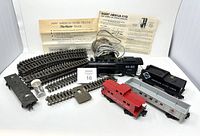 Photo showing engine, 3 cars, transformer, and various curved and straight track pieces with instruction sheets behind.