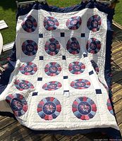 Full view of handmade quilt showing arranged floral circular blocks on white background with navy blue border, draped over outdoor chair.