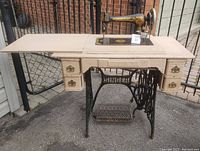 Full view of vintage Singer treadle sewing machine set on painted wood table with five drawers and cast iron treadle base.