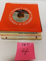 Stack of 25 vinyl 45 RPM records with visible Columbia sleeve on top and pink note indicating Set 4