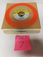 Stack of 25 vinyl 45 RPM records with a Capitol sleeve visible on top and pink note indicating Set 7.