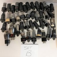 Top-down view of 41 vintage vacuum tubes arranged in rows on a flat surface with a labeled card 'SET B'. Tubes vary in size and markings with multiple brands visible.