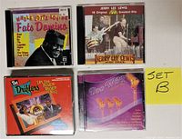Five music CDs including Fats Domino, Jerry Lee Lewis, The Drifters, and Doo Wop compilation, arranged on a flat surface.