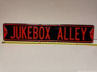 Full front view of the metal sign showing 'JUKEBOX ALLEY' in red raised letters on a black background with a measuring tape below showing length approximately 30 inches.