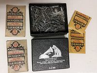 Open RCA Victor black embossed needle box showing assorted metal needles in inner tray along with five Columbia needle packets on the side.