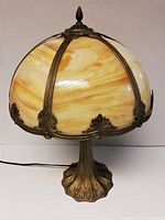 Full view of vintage slag glass lamp showing the dome-shaped glass shade with yellow and amber swirls and iron framework and base.