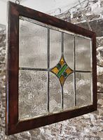 Front view of the rectangular stained glass panel showing the clear textured glass with a central diamond motif of green and amber pieces. Pine frame is visible with wear and dark stain.