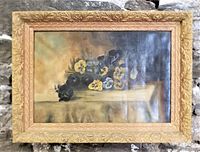 Front view of the antique Victorian oil painting showing pansy flowers and ornate gilt frame hung on a stone wall.