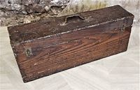 Side view of antique wooden carpenter's tool chest showing dark stained wood, brass handle, and latches.