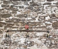 Full view of the Art Deco industrial style light fixture with three black metal wire bulb cages attached to horizontal pipe and red valve handle above.