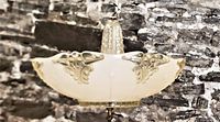 Side angle view of the Art Deco pressed glass ceiling fixture showing peach colored shade with embossed motifs and brass trim.