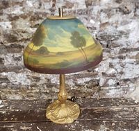 Front view of the Art Deco table lamp showing the reverse painted glass shade with landscape scene and ornate cast metal base.