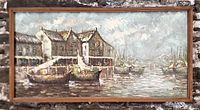 Front view of large landscape-oriented oil painting showing a wharf with buildings and boats in muted colors, framed in a wooden frame with minor edge wear.