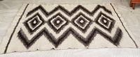 Full view of large vintage thick wool area rug or blanket with geometric diamond pattern in black, grey, and cream tones laid flat on floor.