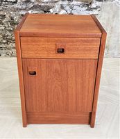 Front view of teak cabinet showing drawer and lower door with inset handles against stone wall background