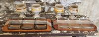Photo showing two teak serving trays each fitted with three square glass dishes and four unique art pottery goblets with fat lava glaze.