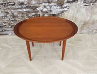 Front three-quarter view of oval teak table against brick wall